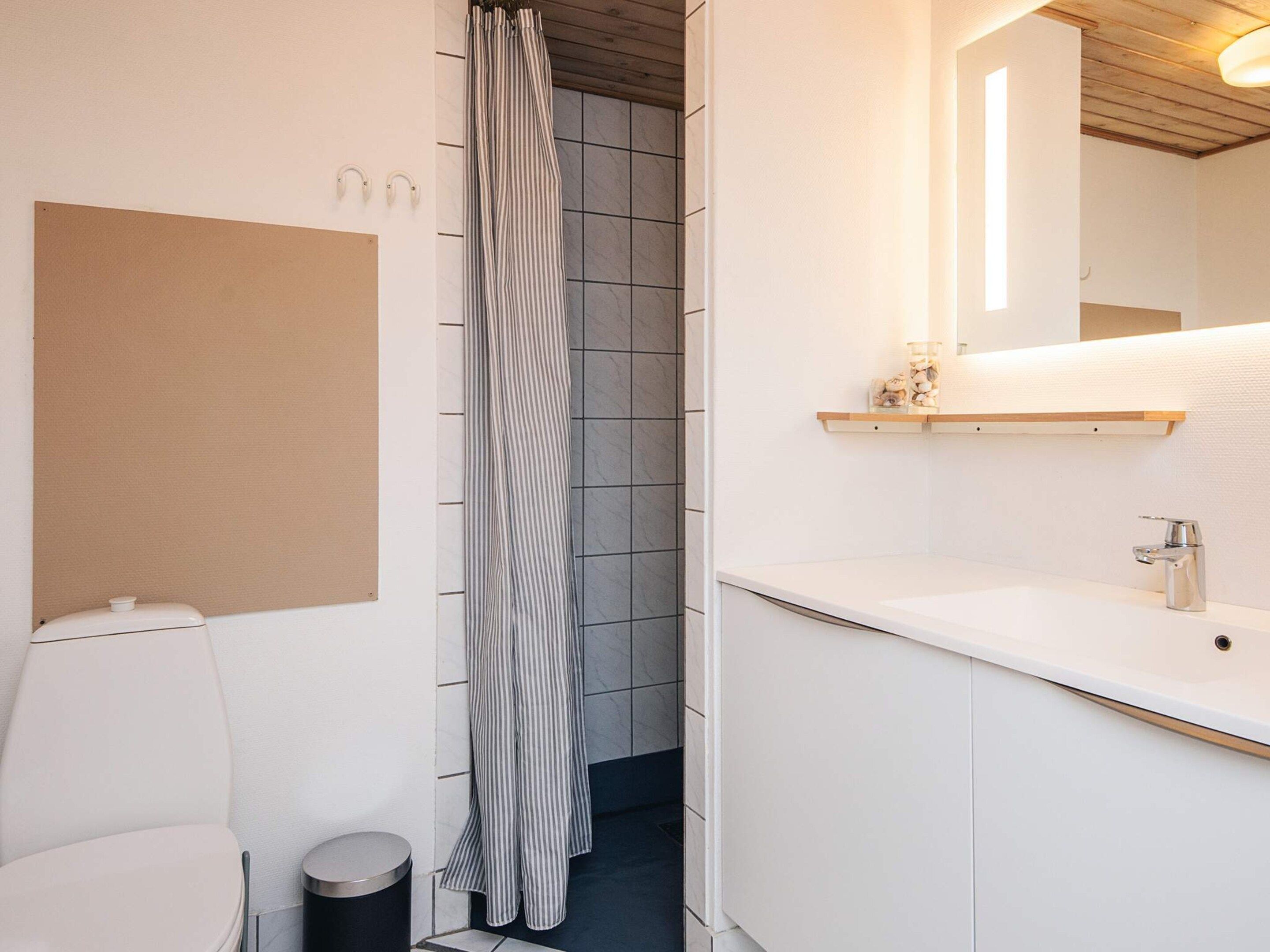 A modern bathroom with a toilet, a sink, a mirror, and a shower curtain.