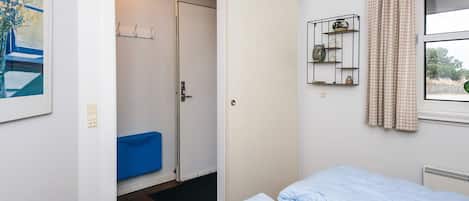 A bedroom with a bed, a door leading to a bathroom, a shelf with decorative items, and a window with curtains.