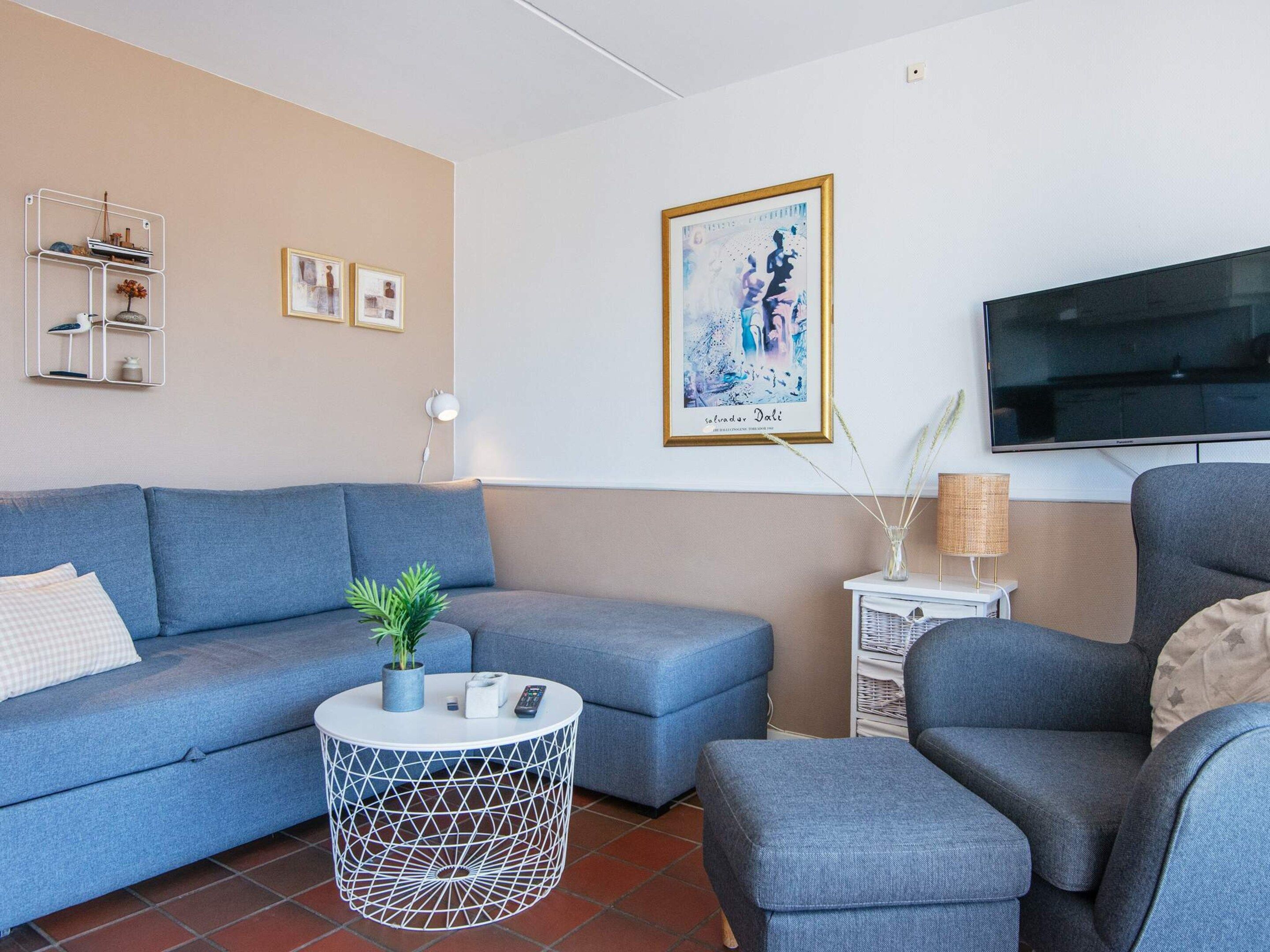 Un salon avec un canapé bleu, une table basse ronde, un téléviseur et un tableau encadré au mur.