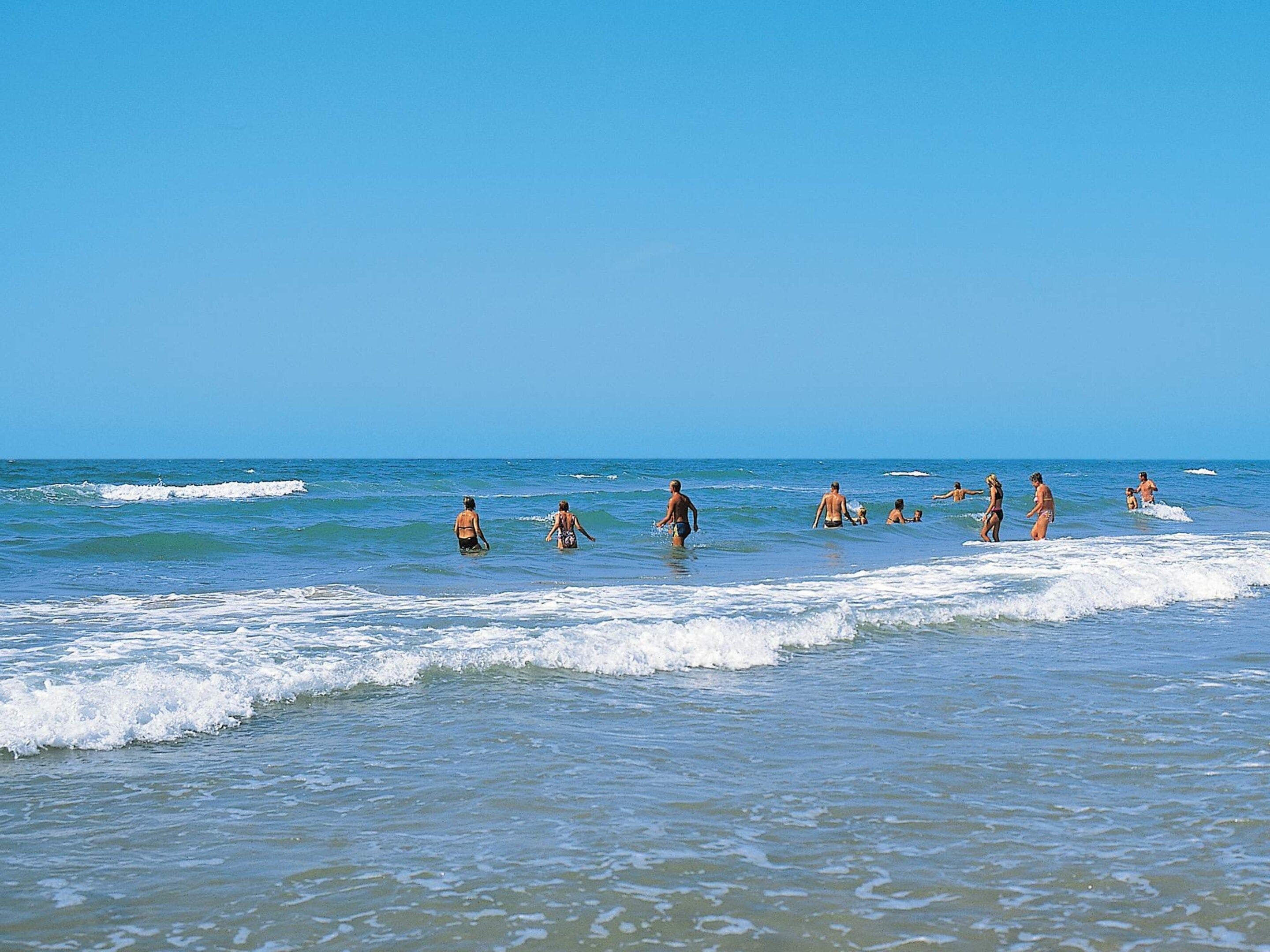 A beach with people swimming and walking in the water.