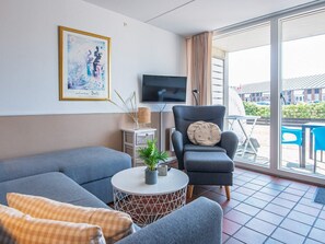 A modern living room with a sofa, armchair, and a small table with a plant. A television is mounted on the wall, and there's a window with curtains. - 4 Person Holiday Home in Fano (Fano)