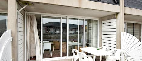 A building with a covered outdoor area featuring a table and chairs, a sliding glass door, and a view of a parking lot.