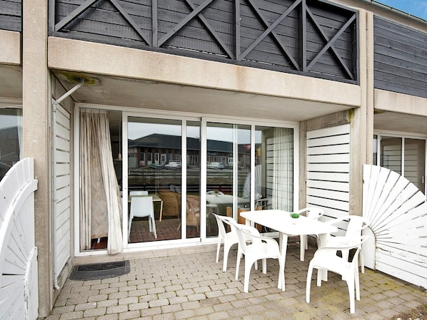 A building with a covered outdoor area featuring a table and chairs, a sliding glass door, and a view of a parking lot.