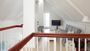 A modern, well-lit living room with a wooden staircase, a grey sofa, a flat-screen TV, and a lamp. - Seaside Escape in Bagenkop - By Traum Ferienwohnungen (Sydlangeland)