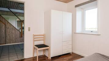 Una habitación con piso de madera, un armario blanco, una silla de madera y una ventana con vistas.