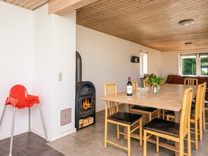 A dining area with a fireplace, wooden chairs, a table, and a red chair.