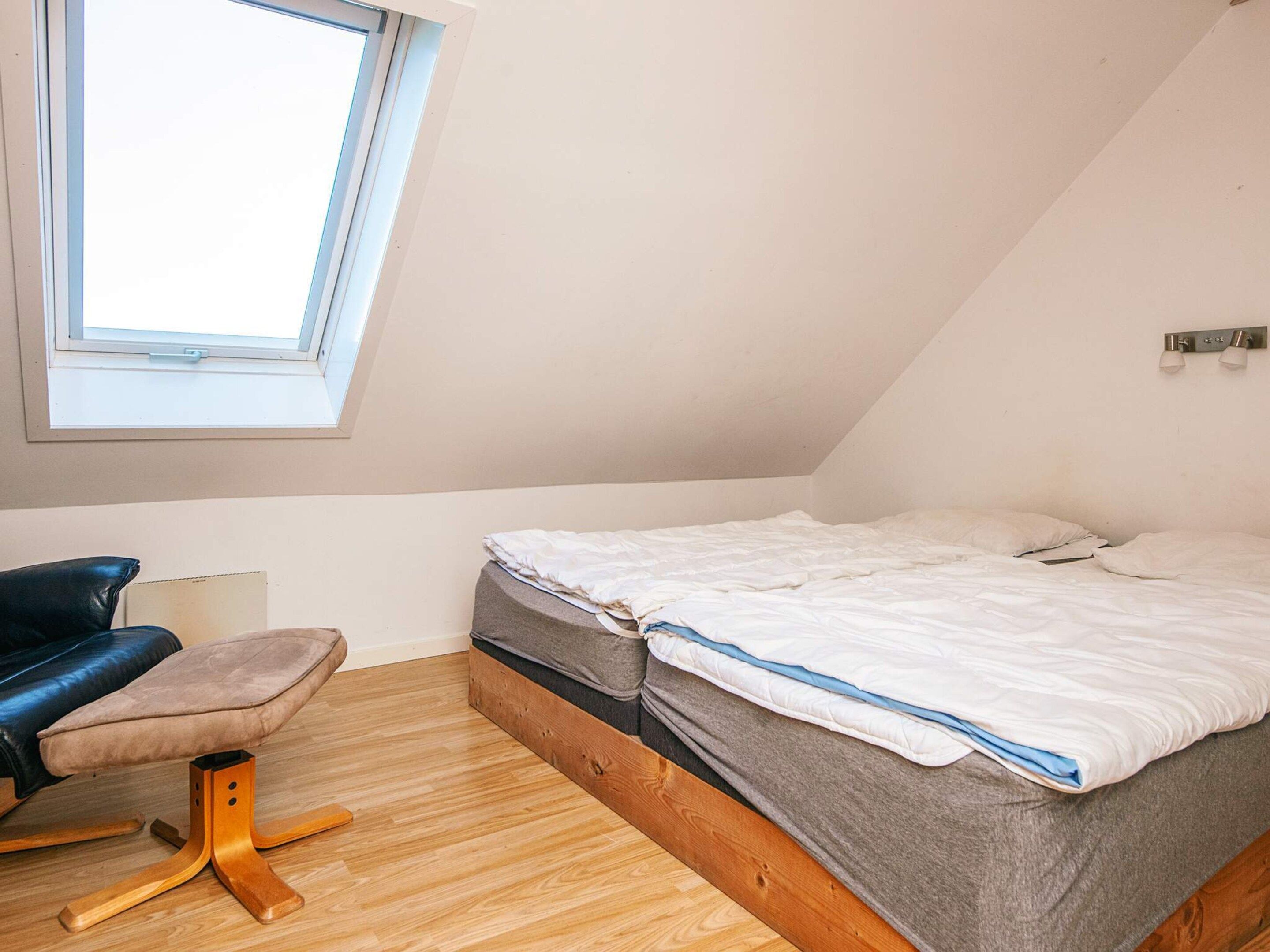 Quarto pequeno com telhado inclinado, uma cama de solteiro, uma escrivaninha e uma cadeira.