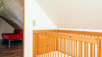 A high-ceilinged room with a wooden crib and a red bench.
