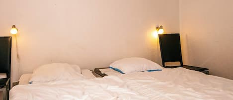 A single bed with white bedding in a room with plain walls and two wall-mounted lamps.