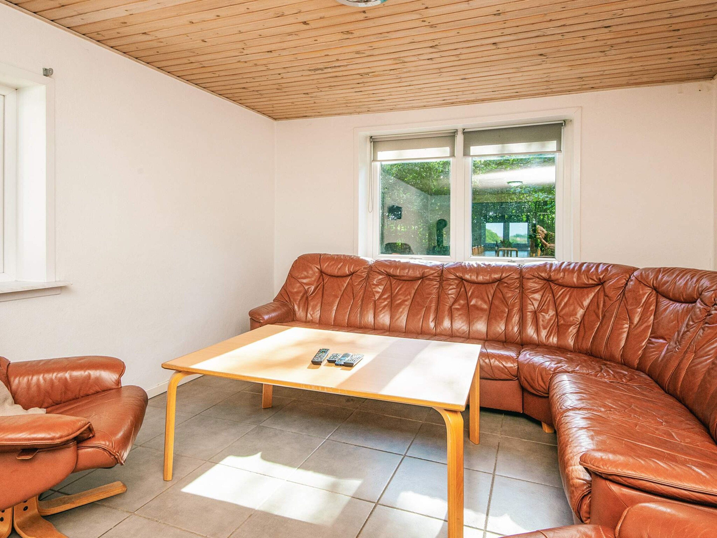 Una habitación con un sofá de cuero marrón, una mesa de centro de madera y una ventana con vistas a zonas verdes.