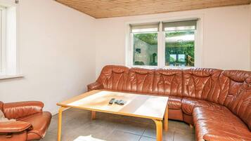 Una habitación con un sofá de cuero marrón, una mesa de centro de madera y una ventana con vistas a zonas verdes.