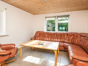 A room with a brown leather sofa, a wooden coffee table, and a window with a view of greenery.