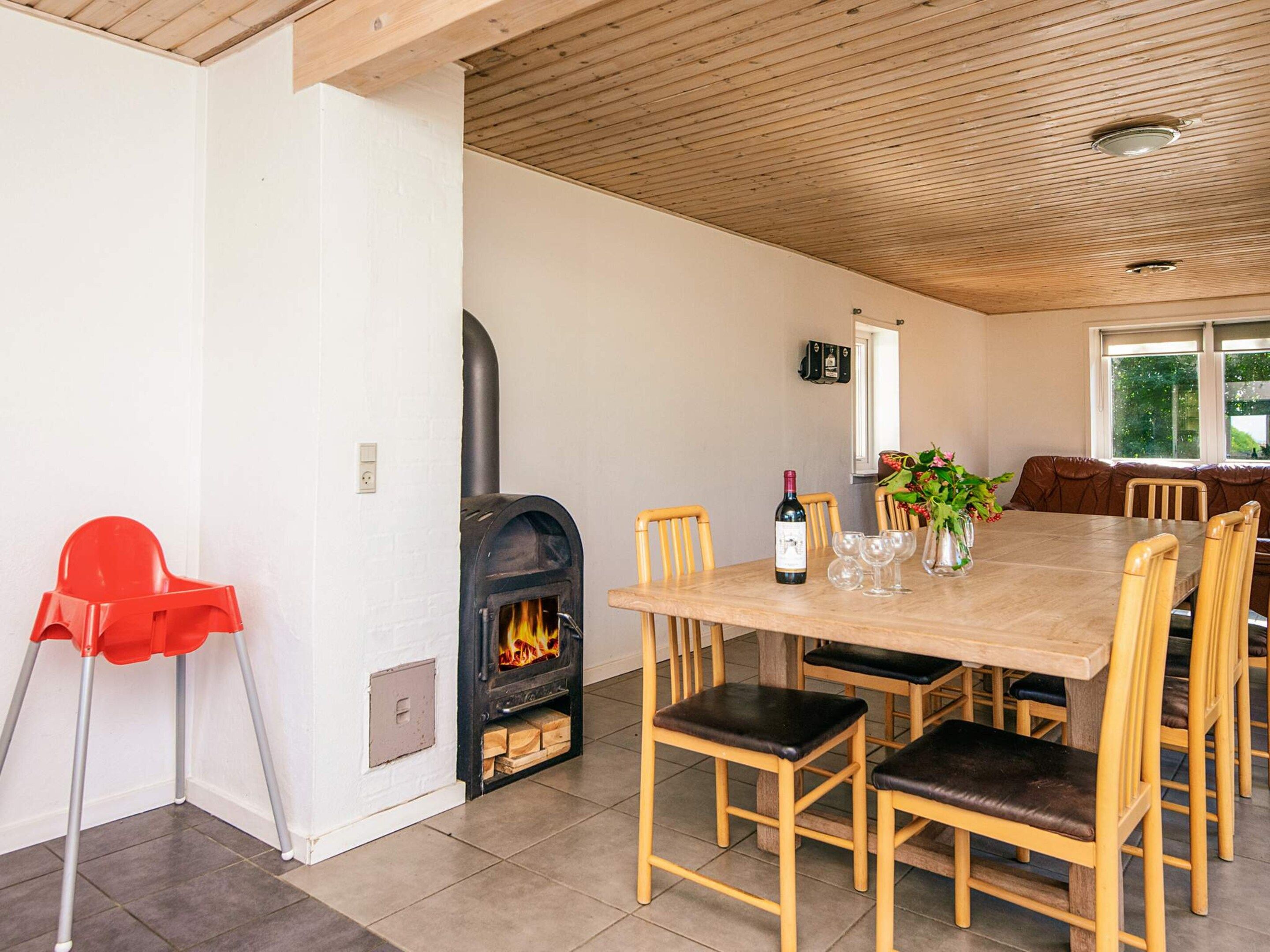 A dining area with a fireplace, wooden chairs, a table, and a red chair.
