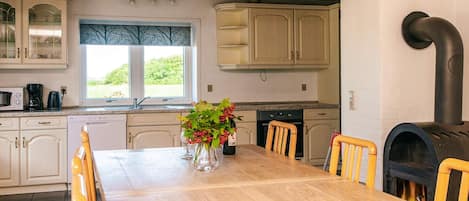 Una cocina con armarios de madera, una mesa de comedor, sillas, un ventanal con vistas y una estufa de leña.