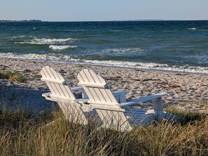 Two white Adirondack chairs on a sandy beach with the ocean in the background. - 12 Person Holiday Home in Bredebro (Bredebro)