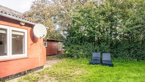 A red building with a satellite dish, a small window, and a grassy yard with two black chairs. - 12 Person Holiday Home in Bredebro (Bredebro)