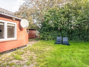 A red building with a satellite dish, a small window, and a grassy yard with two black chairs. - 12 Person Holiday Home in Bredebro (Bredebro)