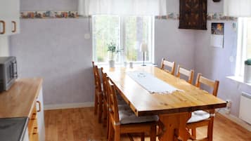 A dining room with a wooden table and chairs, a window with curtains, and a kitchen area with a microwave.