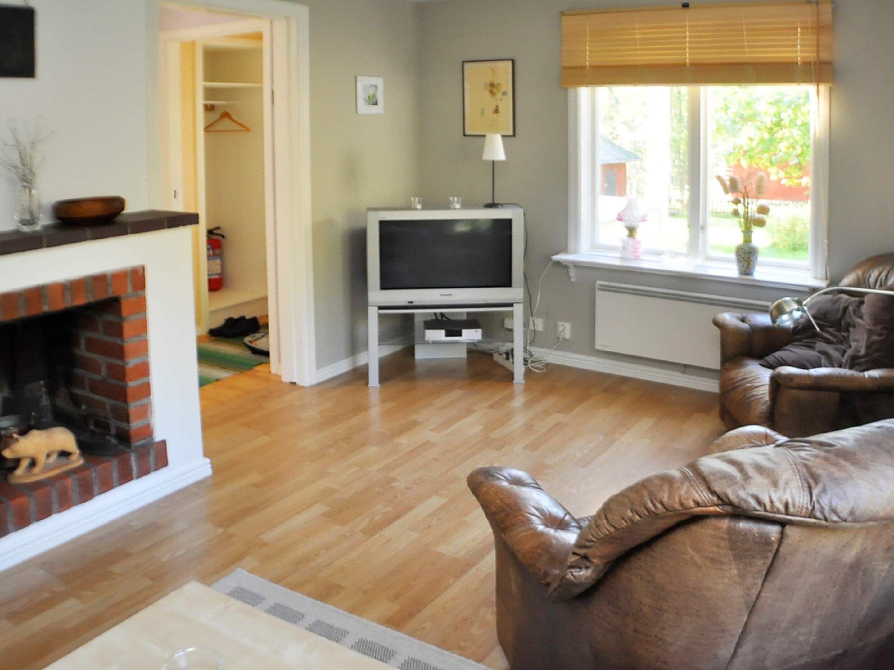 Una sala de estar con chimenea, televisor, ventana con persianas y sofá de cuero.