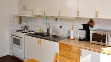 A kitchen with white cabinets, a stove, a sink, a microwave, and a wooden table.