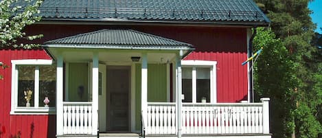 A red house with a porch, a chimney, and a white fence.