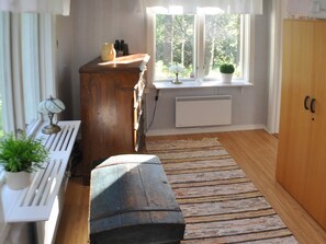 A room with a wooden bench, a radiator, a window with a view of trees, and a cabinet with items on top.