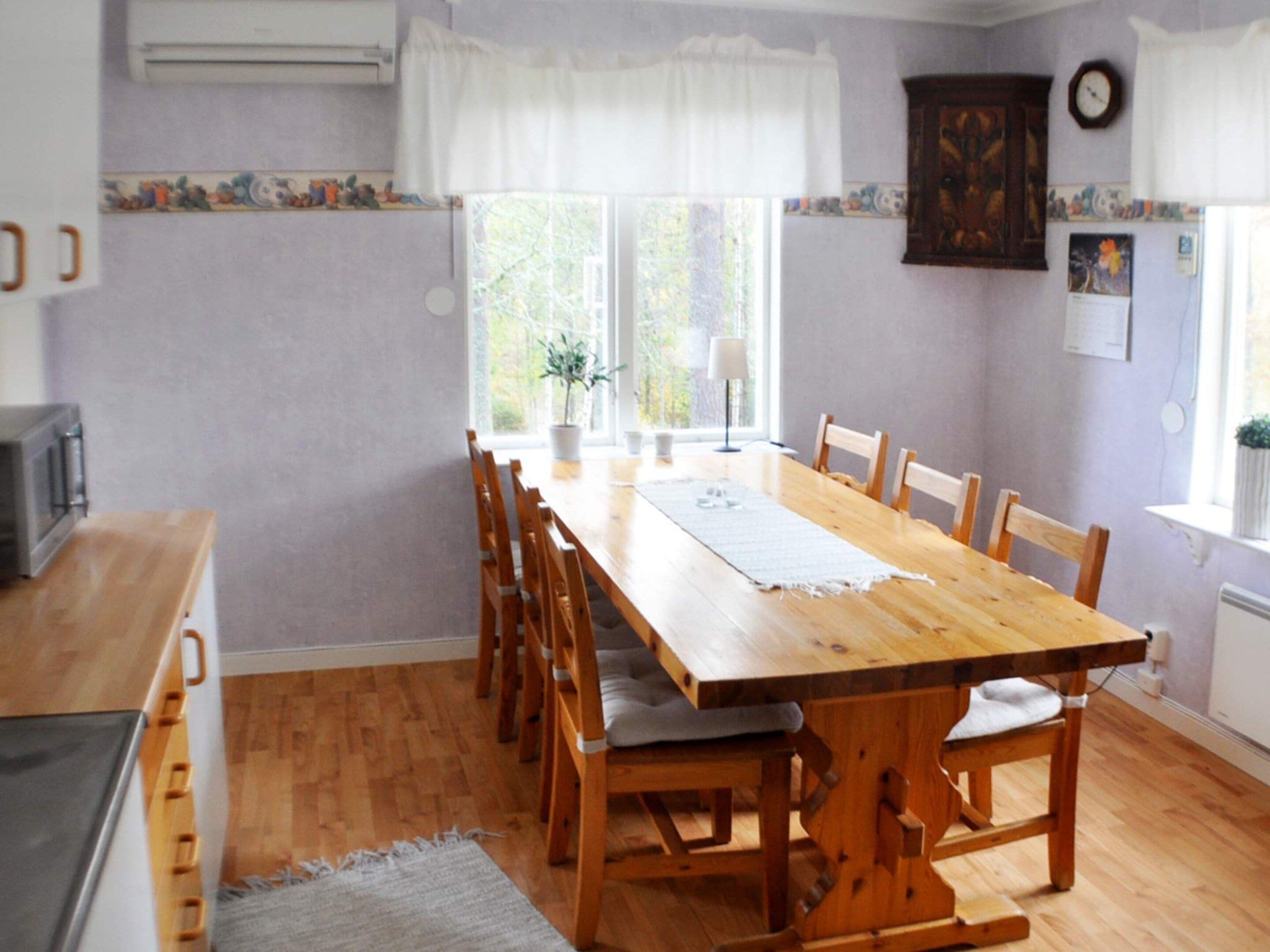 Comedor con mesa y sillas de madera, una ventana con cortinas, y una zona de cocina con electrodomésticos.