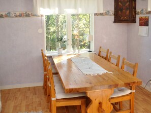 A dining area with a wooden table and chairs, a lace table runner, and a window with a view of greenery. - 5 Person Holiday Home in Arvika (Arvika)