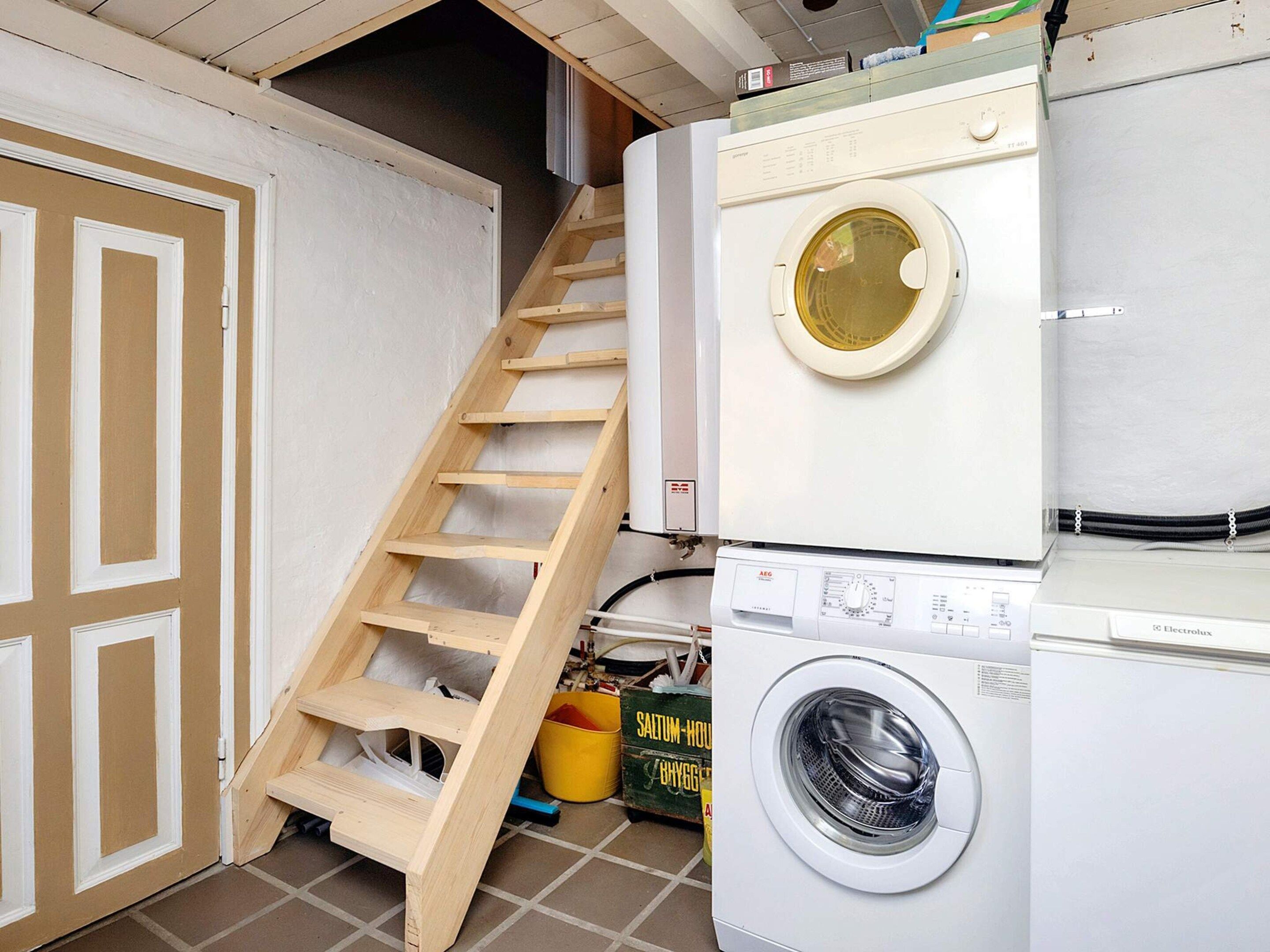 Un lavadero con una escalera de madera que da a un altillo, una lavadora y una secadora.