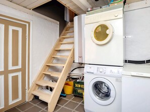 Un lavadero con una escalera de madera que da a un altillo, una lavadora y una secadora.