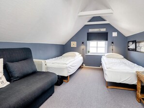Une chambre avec deux lits simples, un canapé, un radiateur, une fenêtre avec des stores et une petite table.