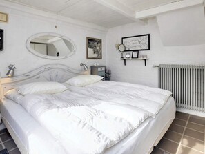 A bedroom with a large bed, a round mirror, a framed picture, a small table with a lamp, and a radiator. - 6 Person Holiday Home in Lokken (Lokken)