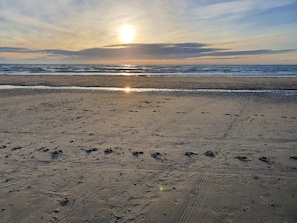 A beach with footprints and tire tracks, a clear sky, and the sun setting or rising. - 6 Person Holiday Home in Lokken (Lokken)