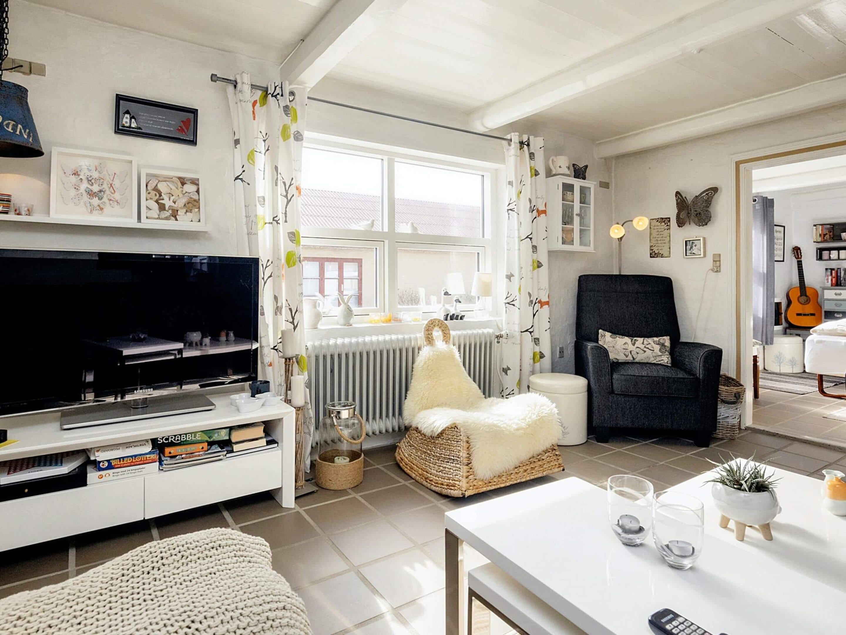 A living room with a television, books, a fireplace, a chair, and a guitar.