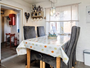 A dining area with a table set for four, a wooden cabinet with bottles, and a window with a curtain. - 6 Person Holiday Home in Lokken (Lokken)