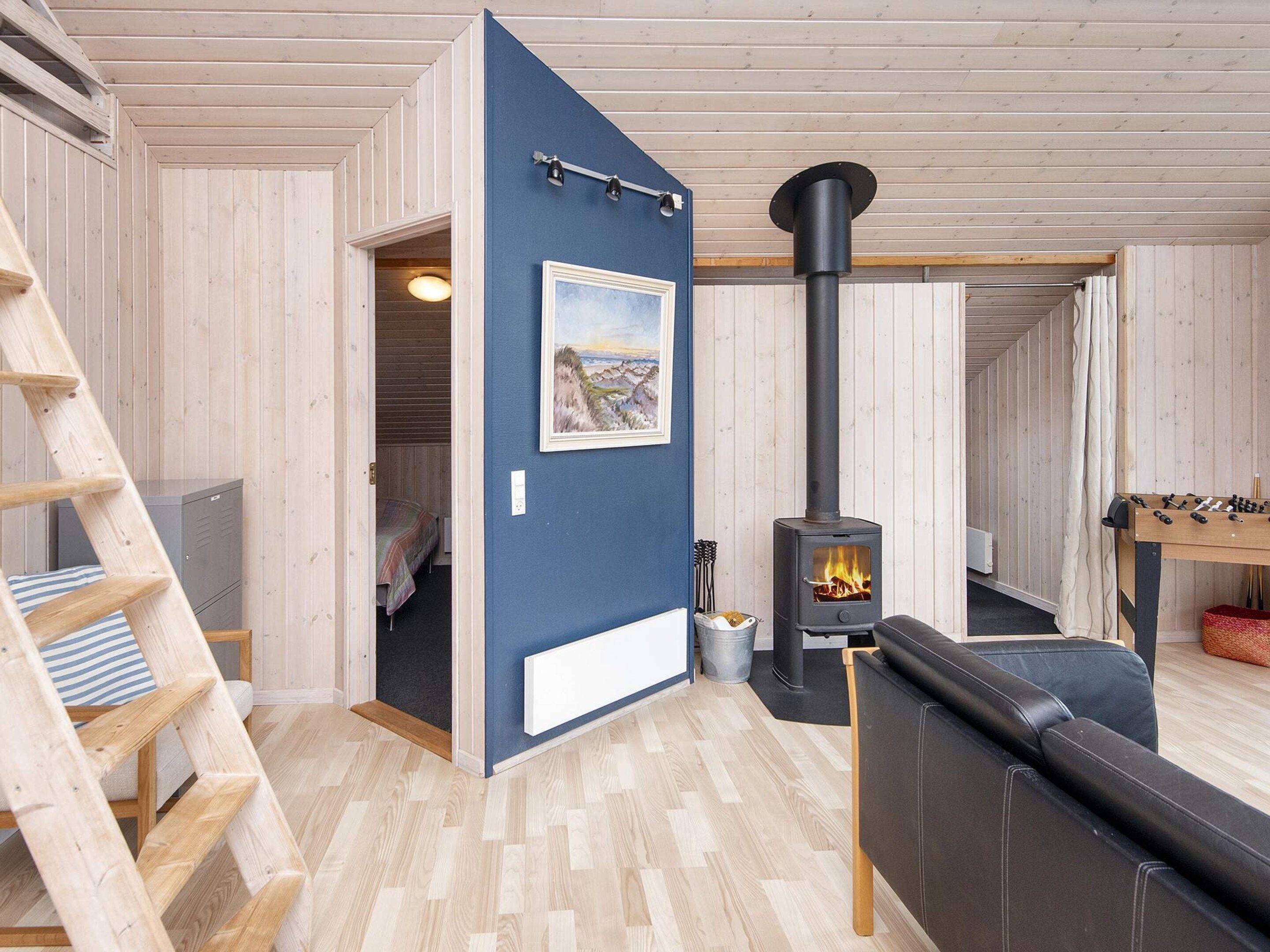 Une pièce chaleureuse avec un décor intérieur en bois, un canapé noir, une échelle en bois, une cheminée et un tableau accroché au mur.
