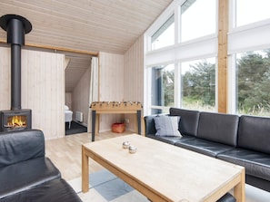 Et hyggeligt værelse med sofa, træbord, et bordtennisbord, pejs og store vinduer.