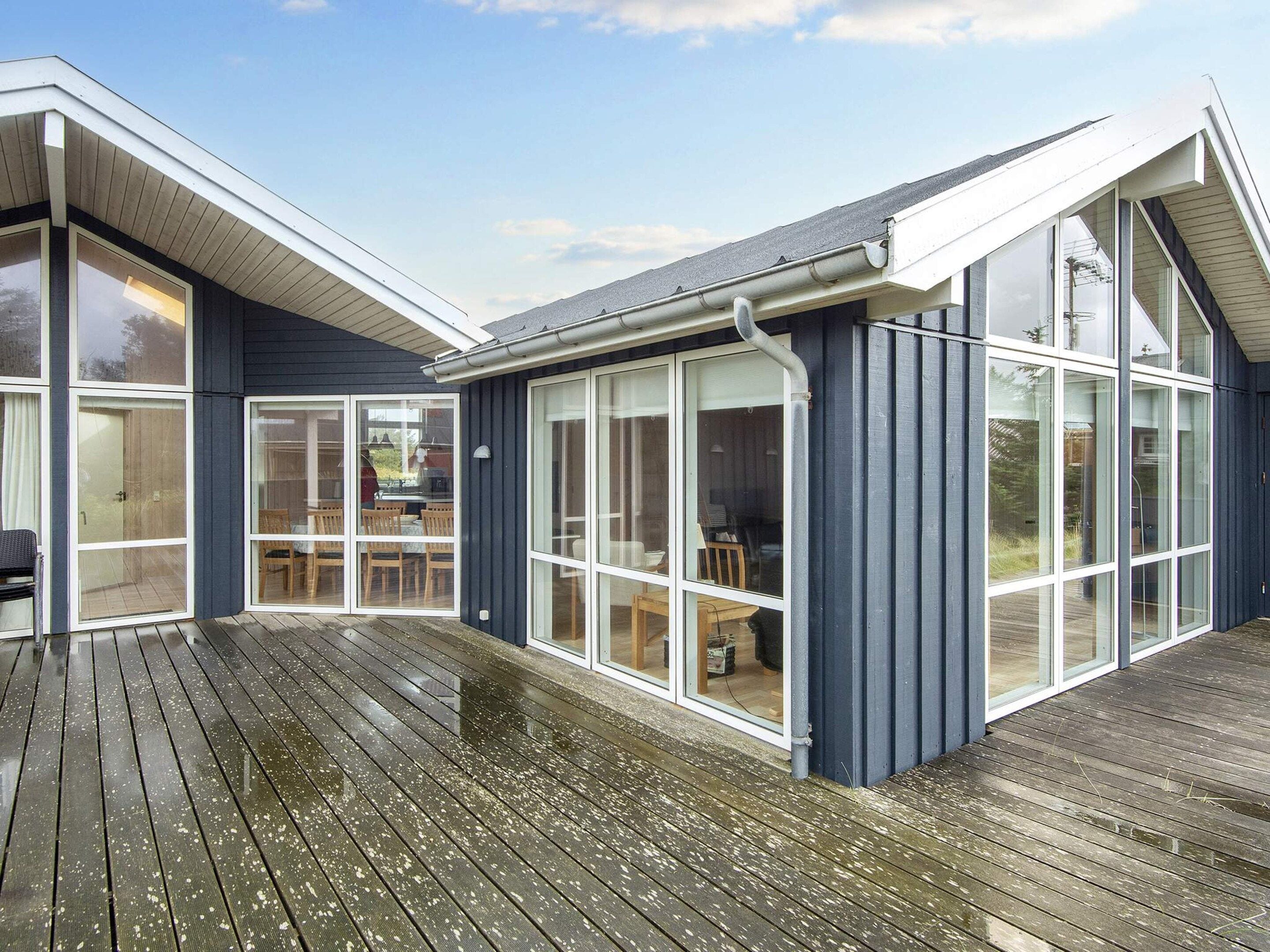 A modern house with large glass windows, a wooden deck, and a covered outdoor area.