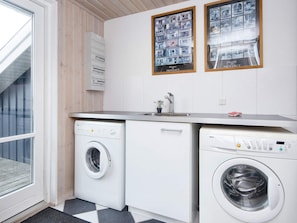 Una sala de bugaderia amb dues rentadores, un bany i una finestra amb vistes a un edifici.