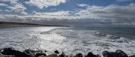 A rocky shoreline with waves, a clear sky, and a distant horizon.