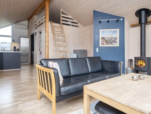A modern living space with a sofa, a wooden table, a fireplace, and a kitchen area. - 5 Star Holiday Home in Harboore (Harboore)