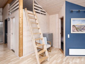 A room with a wooden ladder, a bed, a desk, and a painting on the wall.