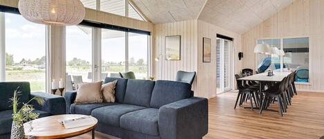 Un interior moderno con un sofá, una mesa de comedor y ventanas amplias.