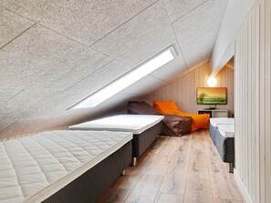 A small, sloped ceiling room with two beds, a bench, and a TV. - 5 Star Holiday Home in Bogense (Bogense)