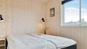 Ein Zimmer mit Holzwandverkleidung, einem Bett mit gemusterten Textilien, einem Nachttisch, einem Fenster mit Blick und einem Wandbild.