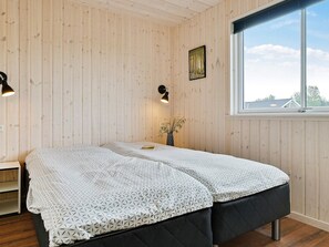 A room with wooden panel walls, a bed with patterned bedding, a bedside table, a window with a view, and a wall-mounted picture. - 5 Star Holiday Home in Bogense (Bogense)