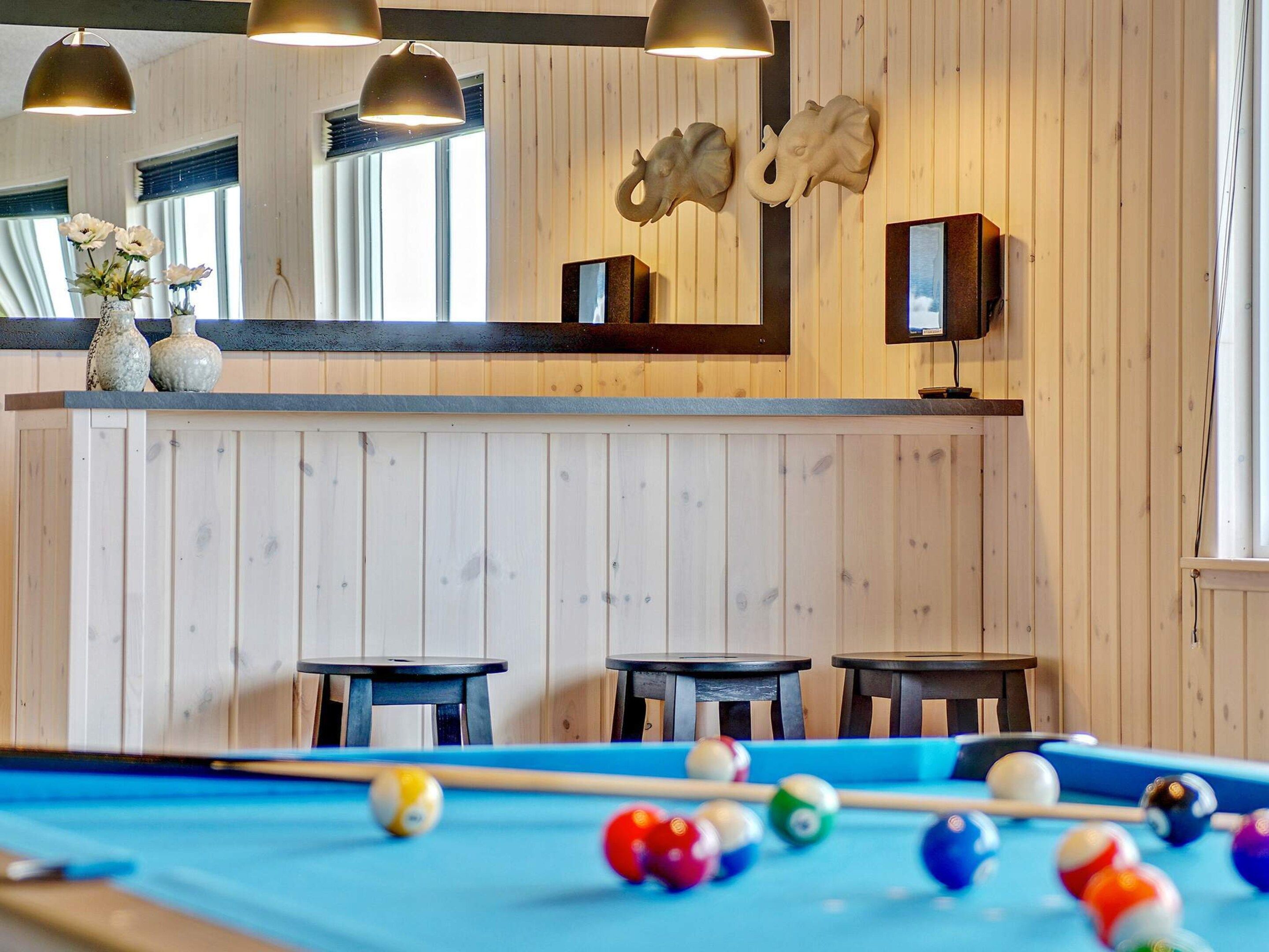 A pool table with balls, wooden walls, and two tables with chairs.