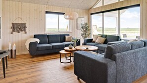 Ein geräumiger Wohnbereich mit großem Fenster, einem dunkelgrauen Sofa, einem runden Couchtisch und Holzboden.
