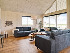 A spacious living area with a large window, a dark gray sofa, a round coffee table, and a wooden floor. - 5 Star Holiday Home in Bogense (Bogense)