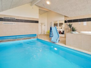 An indoor swimming pool with a blue slide, a sunken seating area, and a small plant on the right.